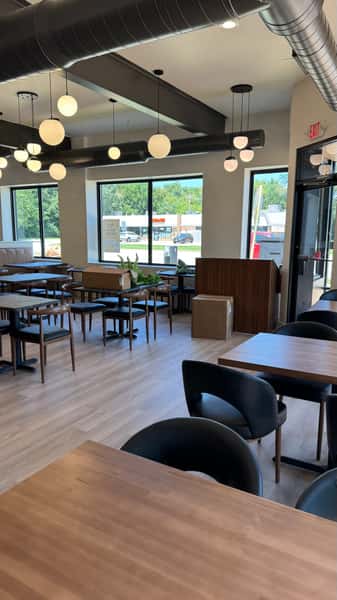 Restaurant seating area with wood flooring, dark chairs, and booths beside large windows
