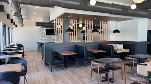 Restaurant dining area with dark blue booth seating, wood tables, and geometric pendant lighting