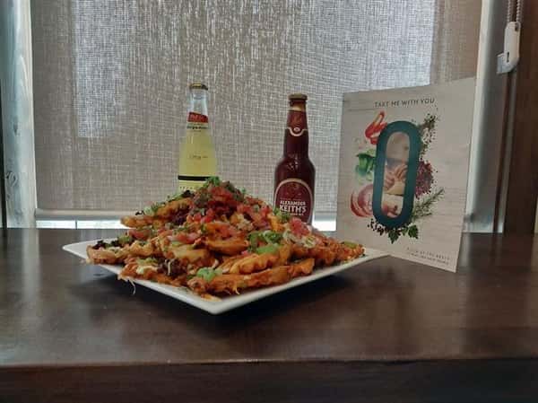 loaded french fries on a plate with bottled beer