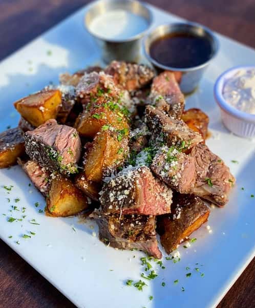 Cubed meat meal, seasoned and covered with garnish served with sauces
