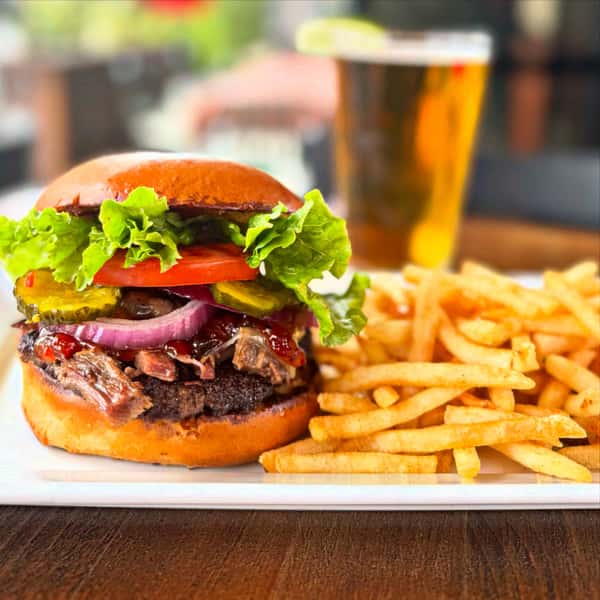 Meat filled burger containing onions, tomatoes, and lettuce, with a side of fries and a drink