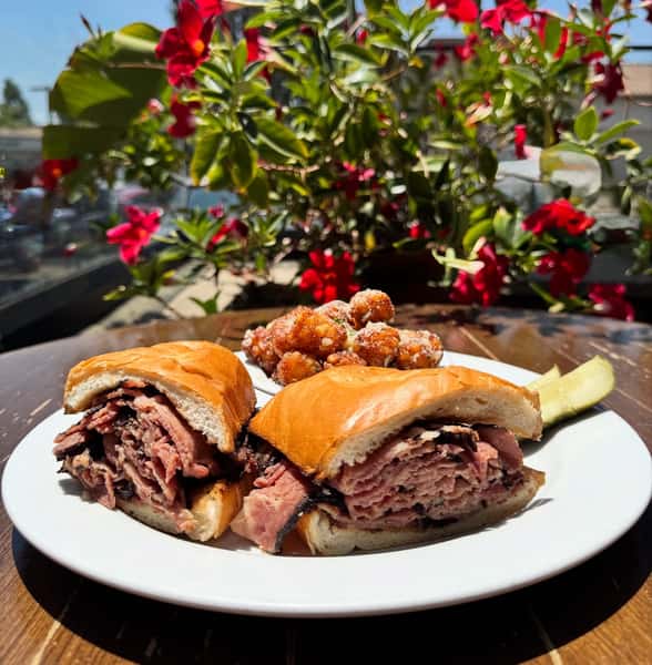 Meat sandwiches on an outdoor table with a plant behind it