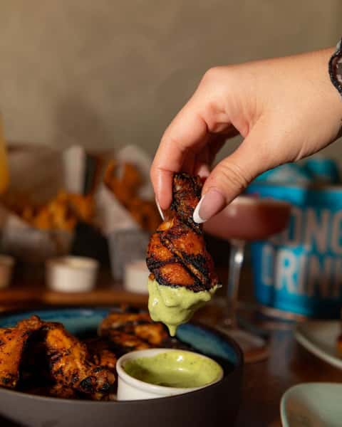 Woman's hand dipping grilled chicken into a green sauce