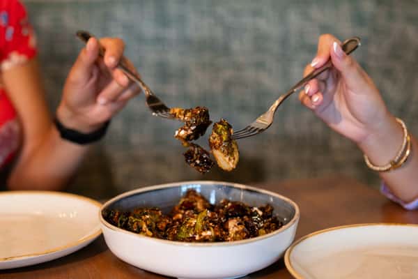 Two hands holding forkfuls of roasted brussel sprouts