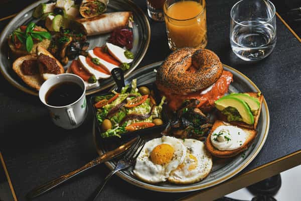Two plates of brunch foods on a table with coffee, water, and juice