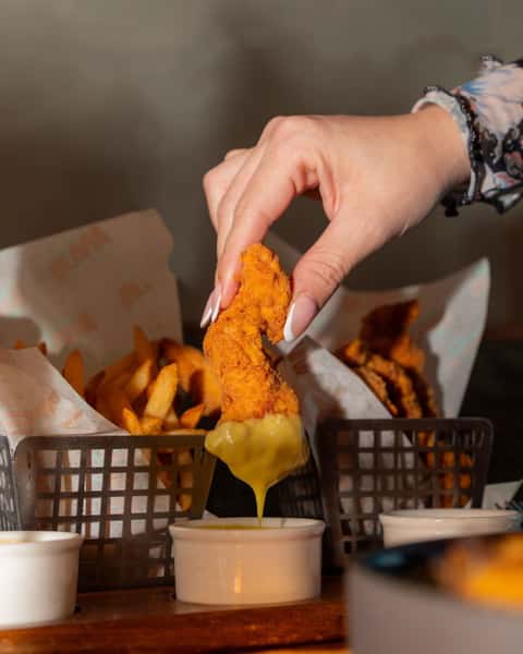 Woman's hand dipping a chicken tender in mustard sauce