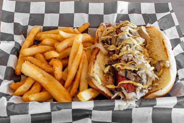 A New York-style hot dog topped with sauce and garnish, served alongside a side of French fries in a paper-lined basket.
