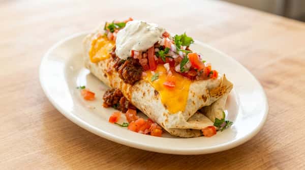 Burrito topped with melted cheddar, ground meat, pico de gallo, and sour cream on a white plate.