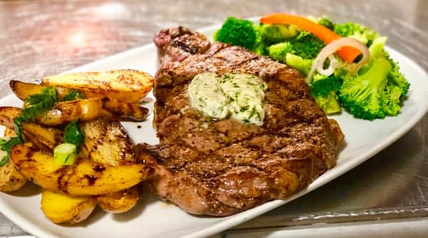 Grilled steak with herb butter, roasted potatoes, and steamed broccoli, garnished with sliced onion and red pepper.