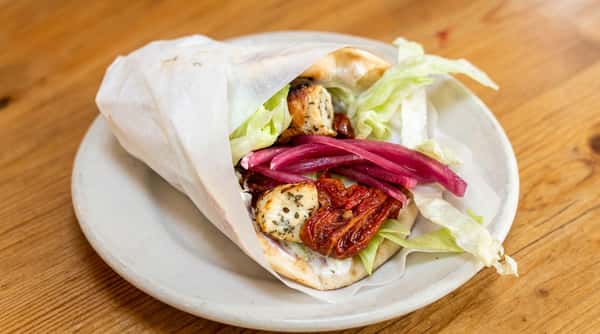Pita bread wrap with grilled chicken, sun-dried tomatoes, pickled red onions, and lettuce on a white plate.