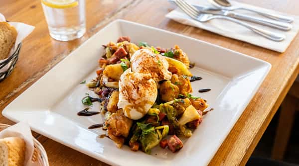 Hash with two poached eggs topped with paprika, on a white rectangular plate with a balsamic glaze drizzle.