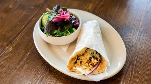 Gyros with white sauce and red onion, wrapped in paper, and a side salad with pickled red onions.