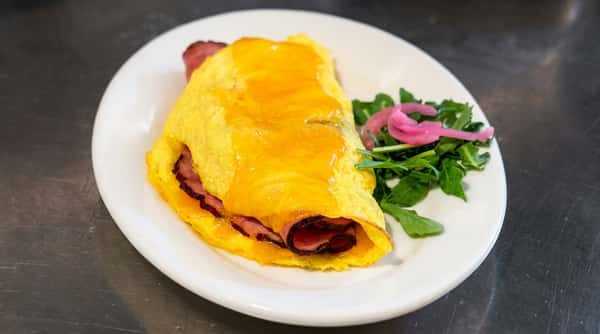 Omelet with melted cheddar cheese and ham filling, served with a side of arugula and pickled red onions.