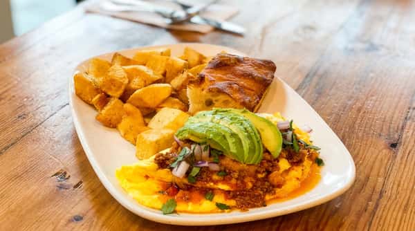 Chili omelette topped with avocado slices, diced red onion, and cilantro, served with home fries and toast.