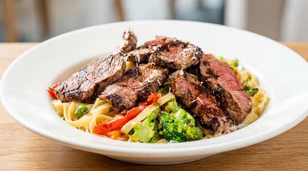 Fettuccine Alfredo topped with sliced steak, broccoli florets, and diced red peppers.