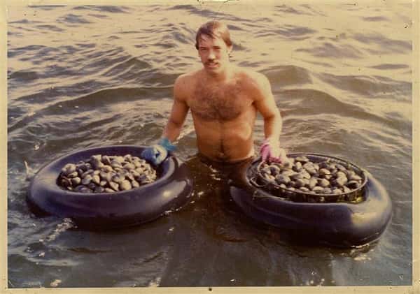 man in water holding buckets of clams