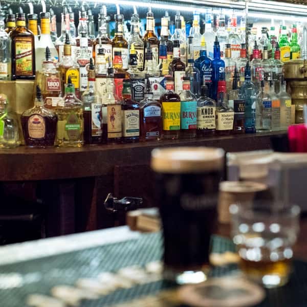 various liquor bottles on the bar with a glass of guinness beer on the bar top