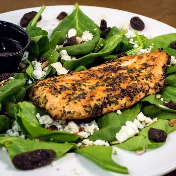 grilled chicken on top of a salad with spinach leaves, craisins, goat cheese and a vinaigrette