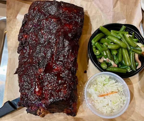 Full rack of glazed barbecue ribs with a caramelized smoky crust, served with a side of tender green beans and creamy coleslaw — a hearty Southern-style BBQ plate packed with flavor.