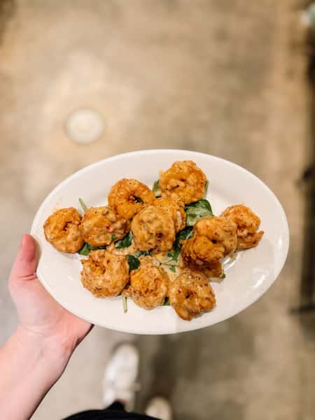 Crispy fried shrimp tossed in a spicy, creamy bang bang sauce, served over greens on a white plate—bold appetizer perfect for Southern and seafood lovers