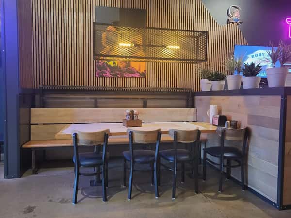 Modern booth seating with wooden accents, black chairs, and potted plants inside a casual barbecue restaurant.