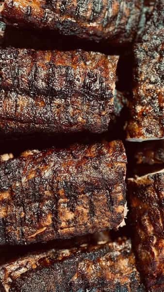 Close-up of perfectly grilled, charred beef ribs with a smoky, caramelized crust, highlighting the rich texture and deep barbecue grill marks — ideal for showcasing a rustic American BBQ or steakhouse vibe.