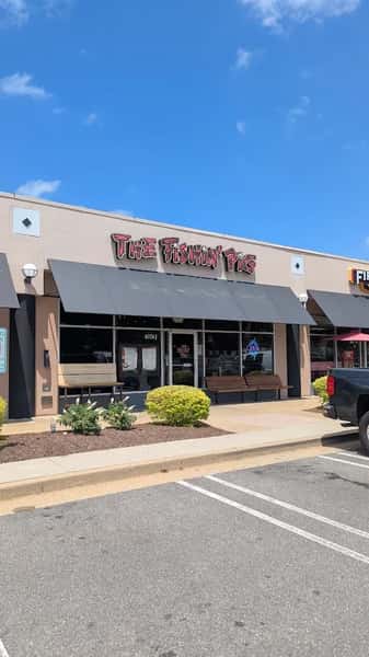 Bright daytime view of The Fishin' Pig restaurant exterior with signage, outdoor bench, and landscaped greenery.