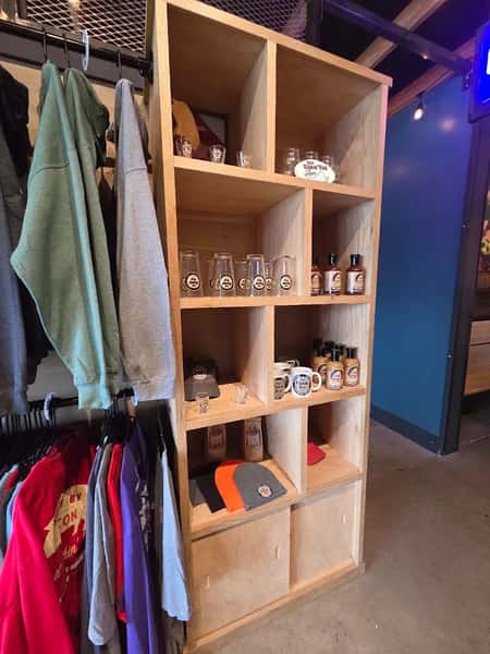 Restaurant merchandise display featuring branded sauces, mugs, glassware, hats, and apparel for sale.