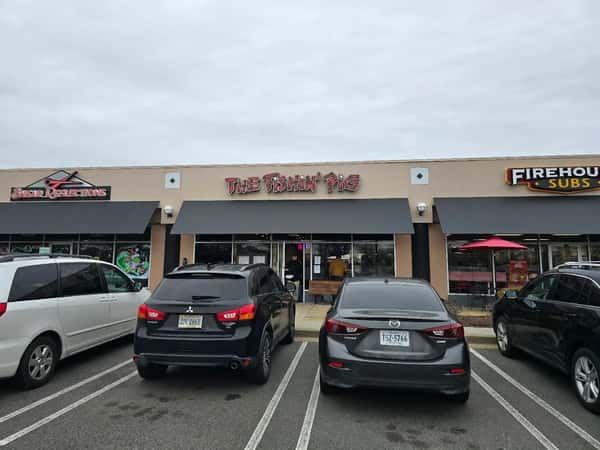 Exterior view of The Fishin' Pig restaurant in a shopping center, with cars parked out front.