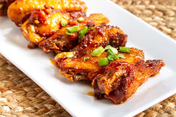 sweet Asian chili wings glazed with sauce and garnished with herbs on a white plate