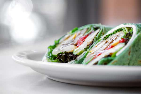 Spinach wrap stuffed with veggies, peppers, and lettuce