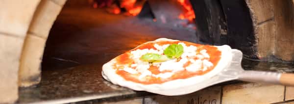A pizza topped with tomato sauce, fresh mozzarella, and basil sitting inside a wood-fired oven.