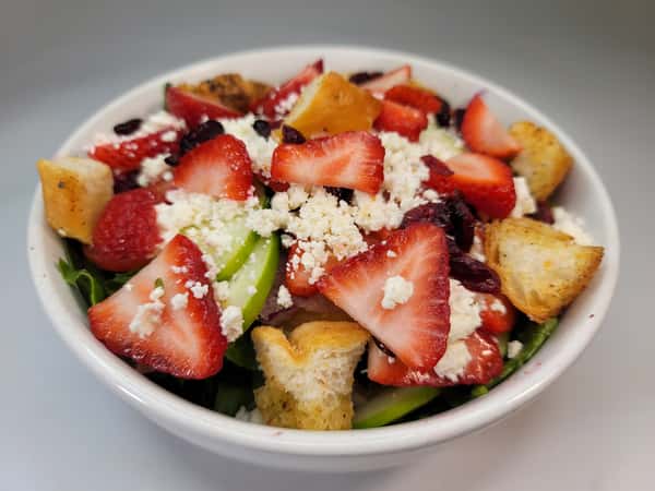 Gasparilla's fresh salad with strawberries, feta cheese, croutons, dried cranberries, cucumber, and greens in a white bowl.