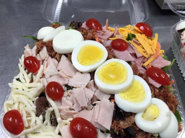 A tray of a our chef salad topped with shredded cheese, eggs bacon and cherry tomatoes