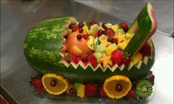 A sculpture of a stroller made from a watermelon, filled with several fruits