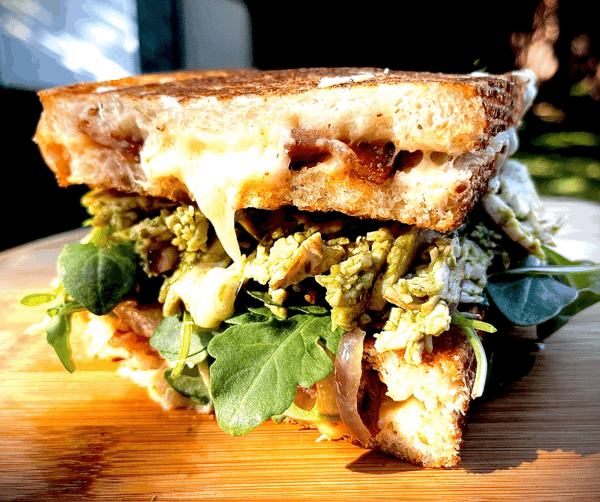 A gourmet pesto chicken and bacon sandwich from The Hungry Deckhand with melting white cheese and fresh arugula on toasted sourdough.