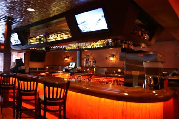 photo of the bar with alcohol stored underneath, televisions, and bar stools around
