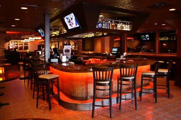 photo of the bar with alcohol stored underneath, televisions, and bar stools around