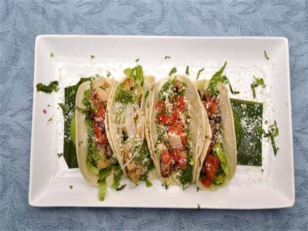 four soft tacos with lettuce, tomatoes, chicken on a plate