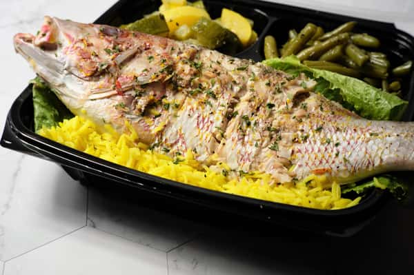 Whole steamed fish seasoned with herbs, served over yellow rice with green beans and sautéed zucchini in a takeout container.