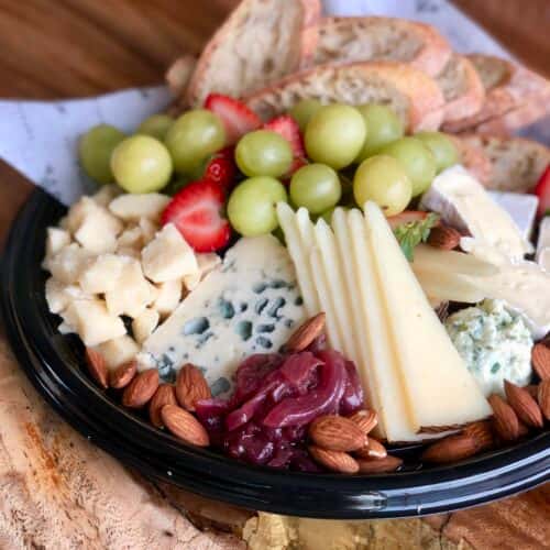 A cheese platter with an assortment of cheeses, including blue cheese and brie, paired with grapes, strawberries, almonds, crackers, and a side of fruit preserve.