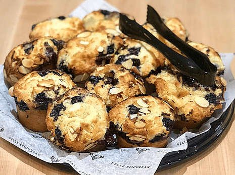 A tray of freshly baked muffins, studded with blueberries and topped with slivered almonds, arranged on parchment paper.