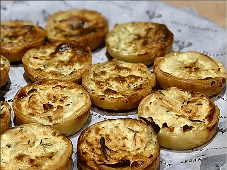 A tray of freshly baked savory pastry tarts, likely filled with cheese and herbs, arranged neatly on parchment paper.