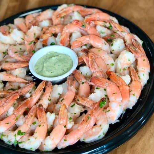 A platter of chilled shrimp arranged in a circular pattern, with a side of dipping sauce in the center.