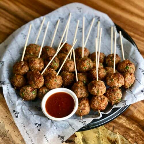 A platter of meatballs on skewers, served with a side of dipping sauce.