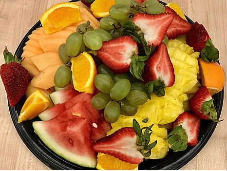 A vibrant fruit platter featuring slices of watermelon, pineapple, orange, strawberries, and grapes, arranged neatly for serving.
