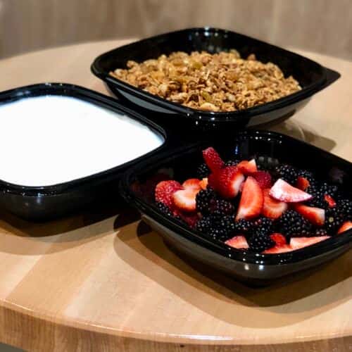 A set of bowls featuring granola, fresh berries (strawberries and blackberries), and a serving of yogurt.