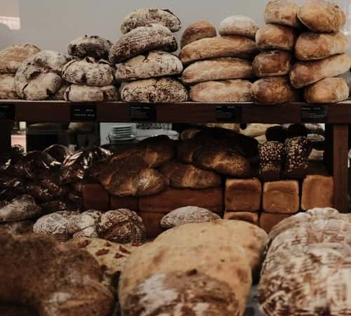 A variety of freshly baked loaves of bread, including round, square, and artisanal styles, stacked neatly on shelves.