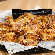 A platter of savory pastries, possibly filled with ham and cheese, arranged on parchment paper with a black tray.