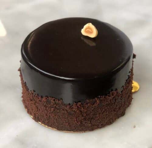 A chocolate cake with a glossy ganache topping, decorated with chocolate drizzle and a coffee bean on top.